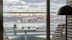 A view from a high-rise building overlooking a cityscape with a river, featuring a table with cups and a chair. - Scandic Alvik (Bromma)