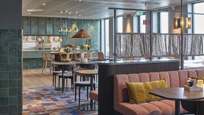 A modern restaurant with a bar area, seating arrangements, and a view through large windows. - Scandic Alvik (Bromma)