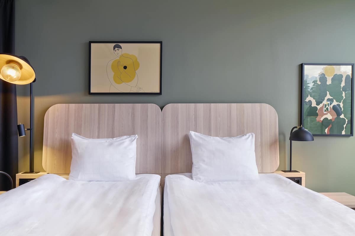 Un lit double avec du linge de lit blanc, une tête de lit en bois et deux tables de chevet avec des lampes.
