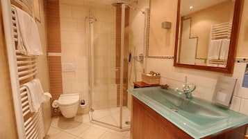 Un baño moderno con lavamanos de vidrio, cabina de ducha y retrete.