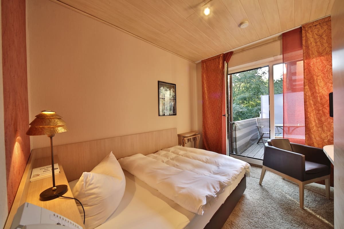 A hotel room with a bed, a desk, a chair, a lamp, and a window with curtains.