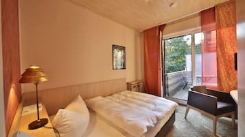 Habitación de hotel con cama, escritorio, silla, lámpara y ventana con cortinas.
