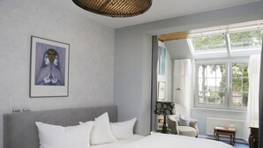 Un dormitorio con una cama grande, una mesita de noche, una silla y una ventana con vistas a árboles.