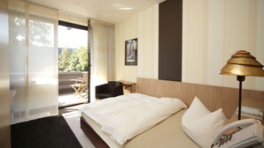 Habitación de hotel con cama, escritorio, silla, lámpara y vistas al exterior.