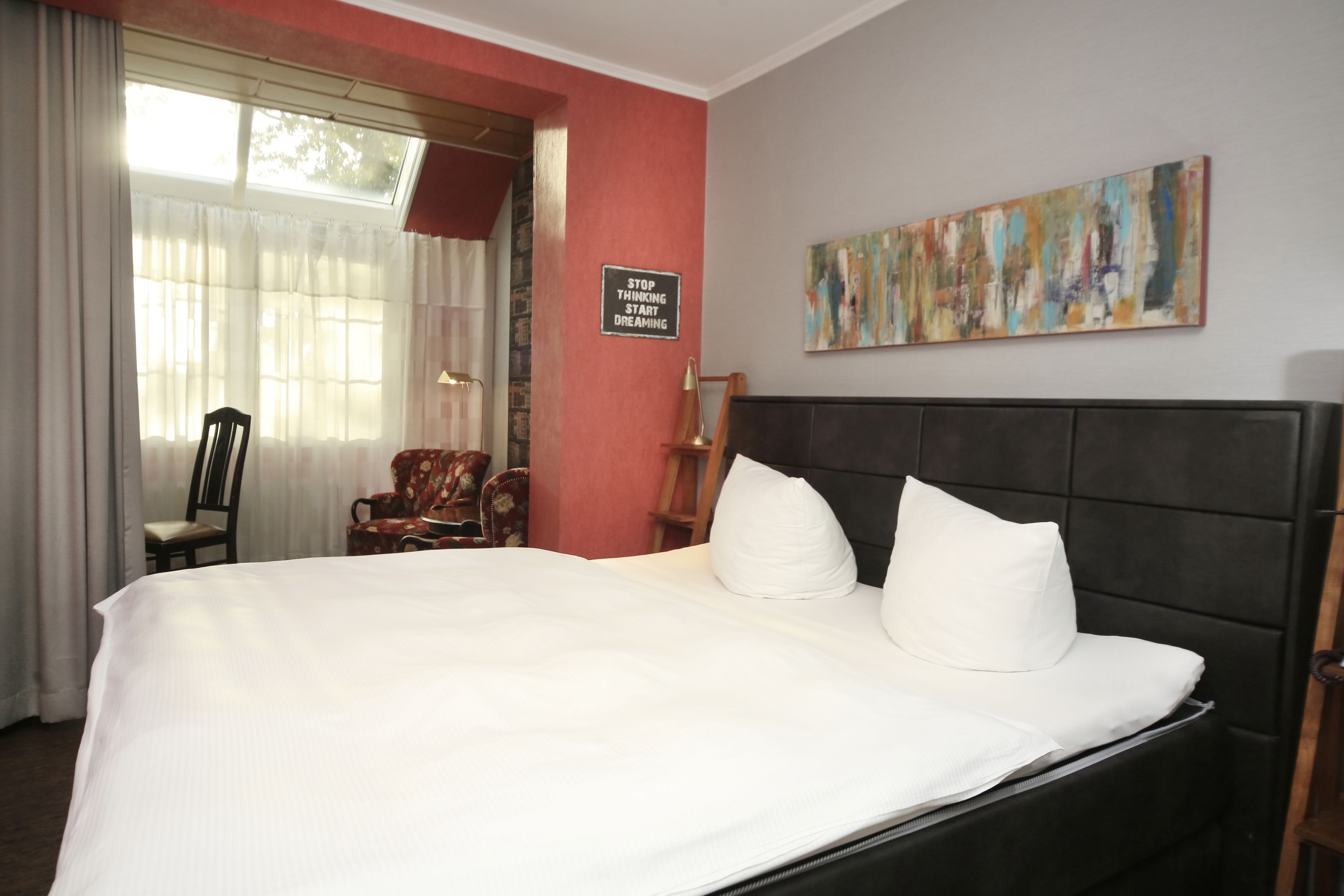 A hotel room with a large bed, a chair, a desk, and a painting on the wall.