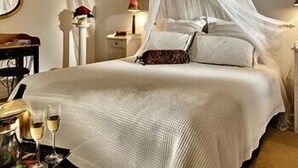 Ein Schlafzimmer mit einem Himmelbett, Nachttischen, einem Spiegel und einem Tablett mit Gläsern.
