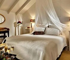 Un dormitorio con cama a dosel, mesitas de noche, un espejo y una bandeja con vasos.