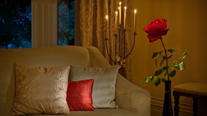 Ein Sofa mit gemusterten Kissen, eine Kandelaber mit brennenden Kerzen und eine rote Rose in einer Vase.