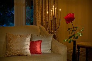 Un sofá con cojines estampados, un candelabro con velas encendidas y una rosa roja en un jarrón.
