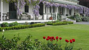 Une maison blanche de style colonial, dotée d’un porche abrité, de mobilier d’extérieur et d’une pelouse bien entretenue agrémentée de tulipes rouges.