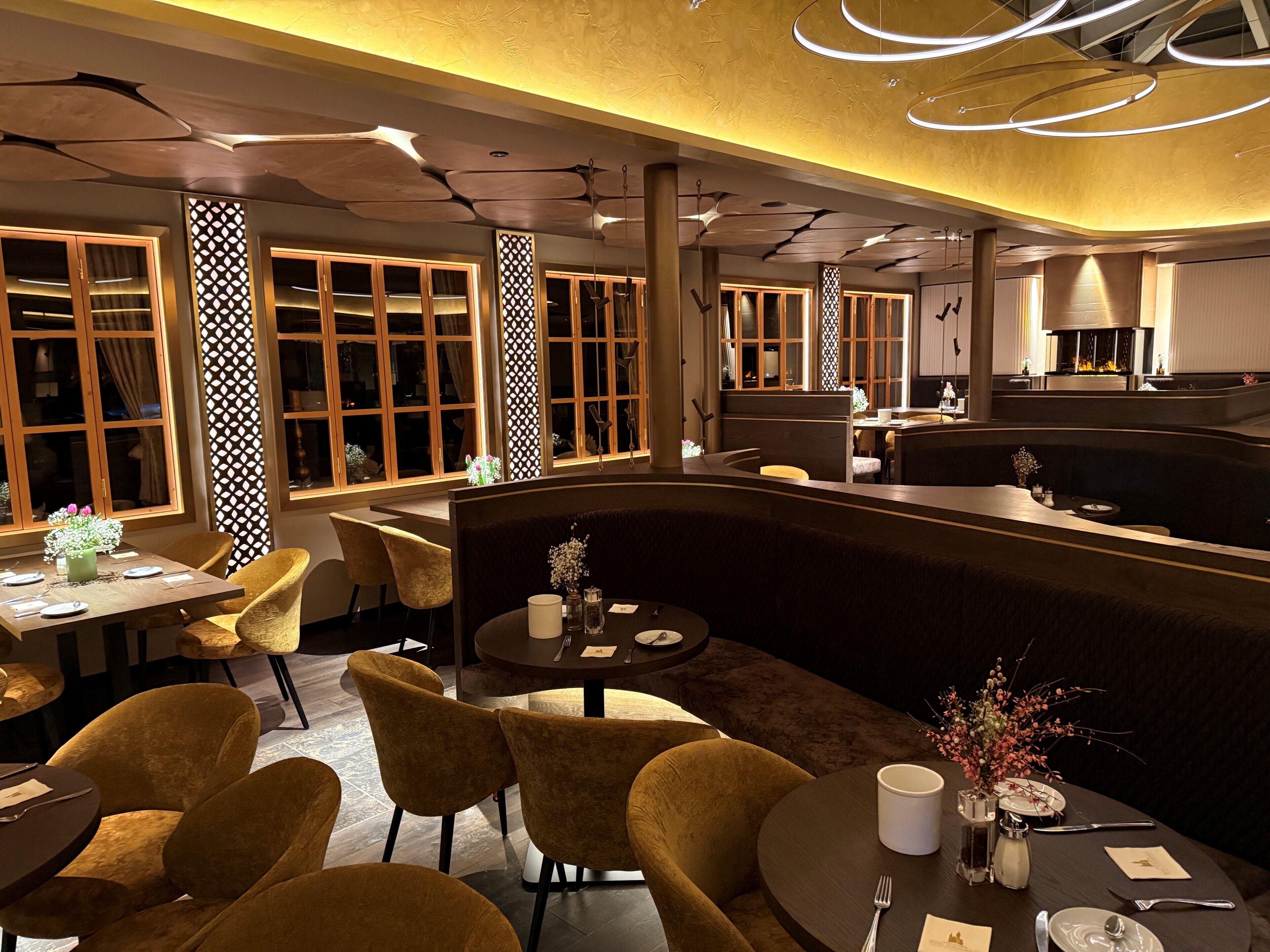 A modern restaurant with round tables, cushioned chairs, and a central bar area.