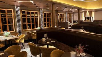 A modern restaurant with round tables, cushioned chairs, and a central bar area.
