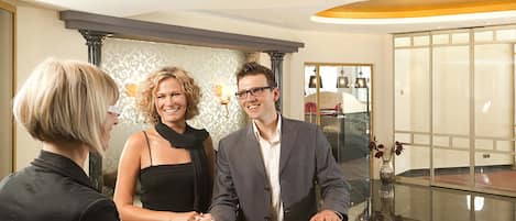 A reception desk with a modern design, a glass partition, and a view of a room with a bed and a window.