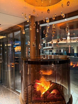 A glass fireplace with a fire, surrounded by hanging crystal ornaments. - Hotel Schlosskrone (Fuessen)
