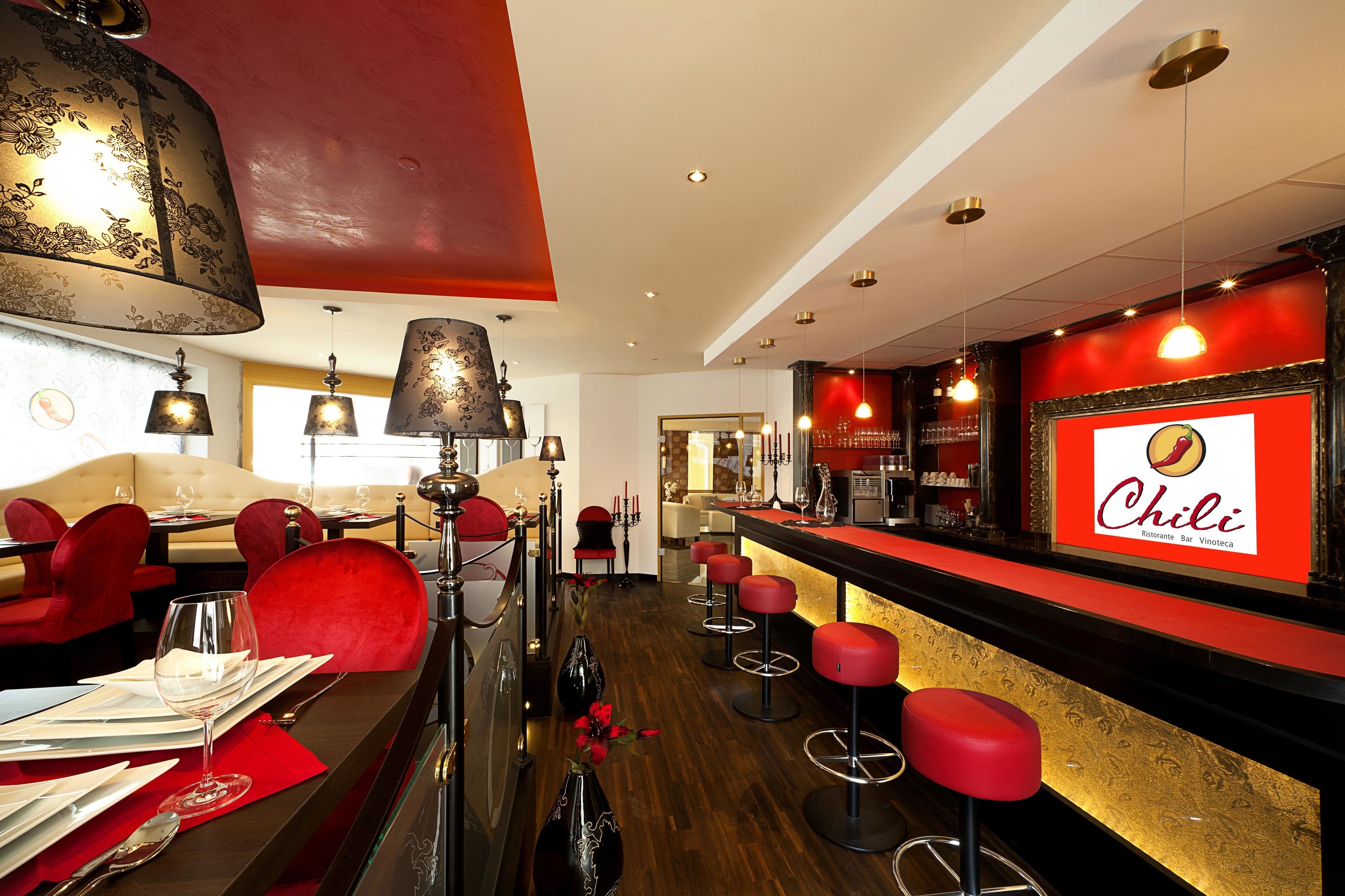 Een restaurantinterieur met rode bekleden stoelen, een bar met krukken en een opvallend 'Chili'-bord.