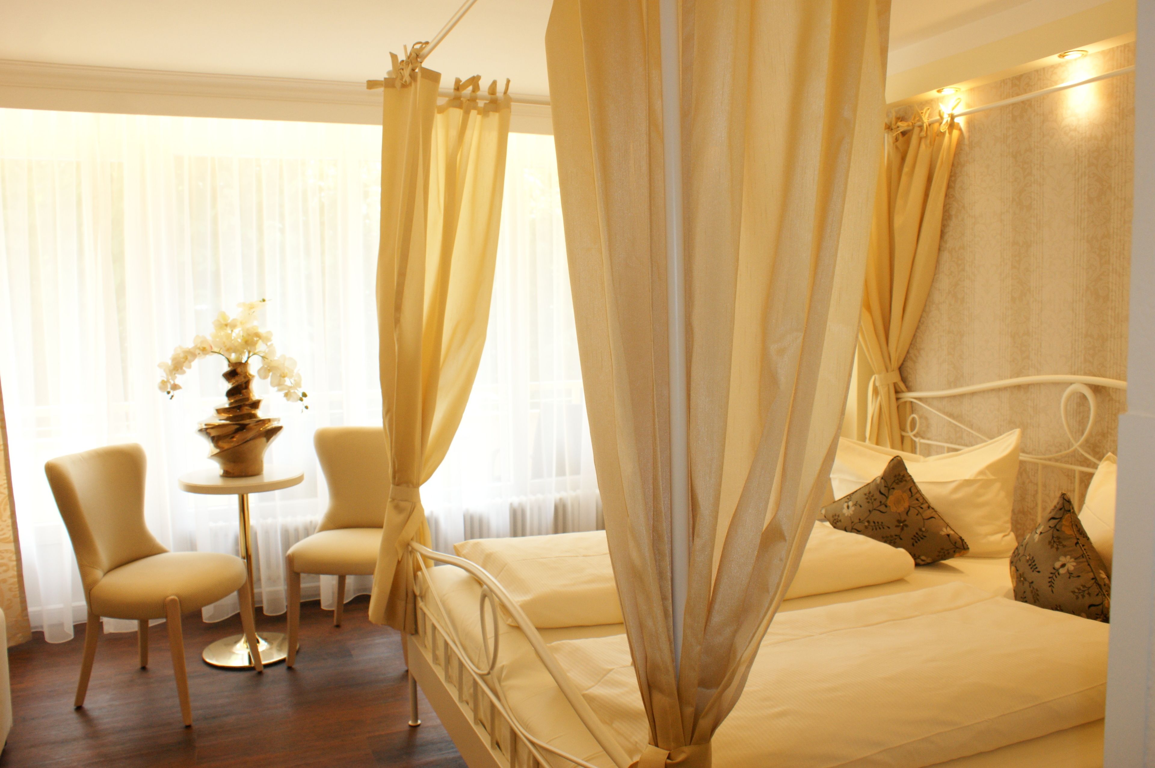 A hotel room with a bed, two chairs, a small table, and a vase of flowers.