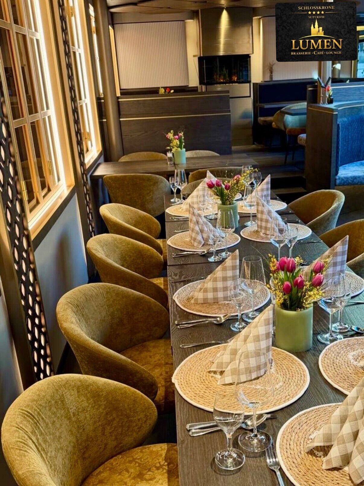 Un ambiente de restaurante con una larga mesa dispuesta para comer, sillas con acolchado y un jarrón decorativo con flores.