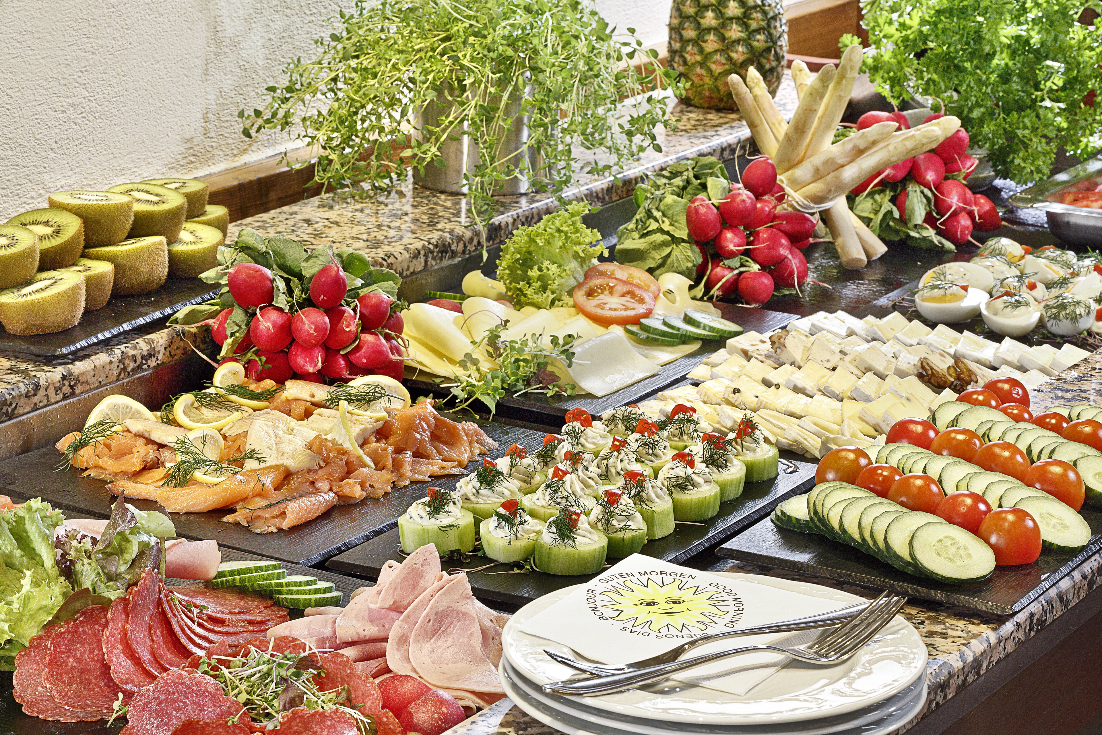 Un bufé con una variedad de alimentos, incluyendo carnes, quesos, frutas y verduras.