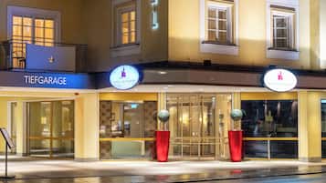 A hotel facade with a sign reading 'TIEFGARAGE HOTEL SCHLOSSBRUNE,' large windows, and two red planters.