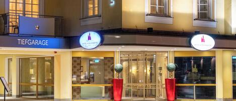 Fachada de un hotel con un letrero que dice 'TIEFGARAGE HOTEL SCHLOSSBRUNE', ventanas amplias y dos macetas rojas.