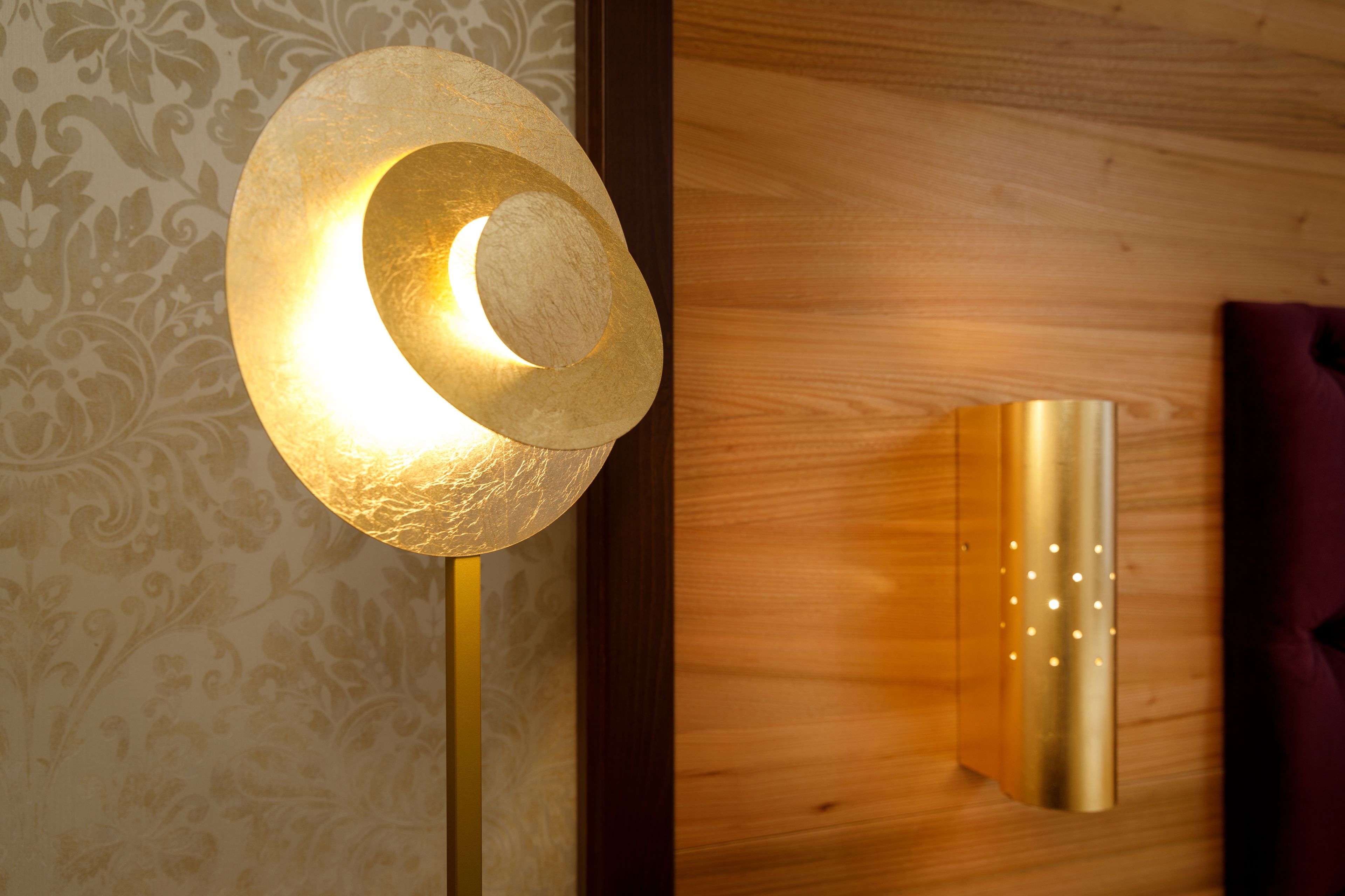 A wall-mounted light fixture with a crescent shape and a cylindrical base, and a vertical light fixture with a cylindrical base and small lights.