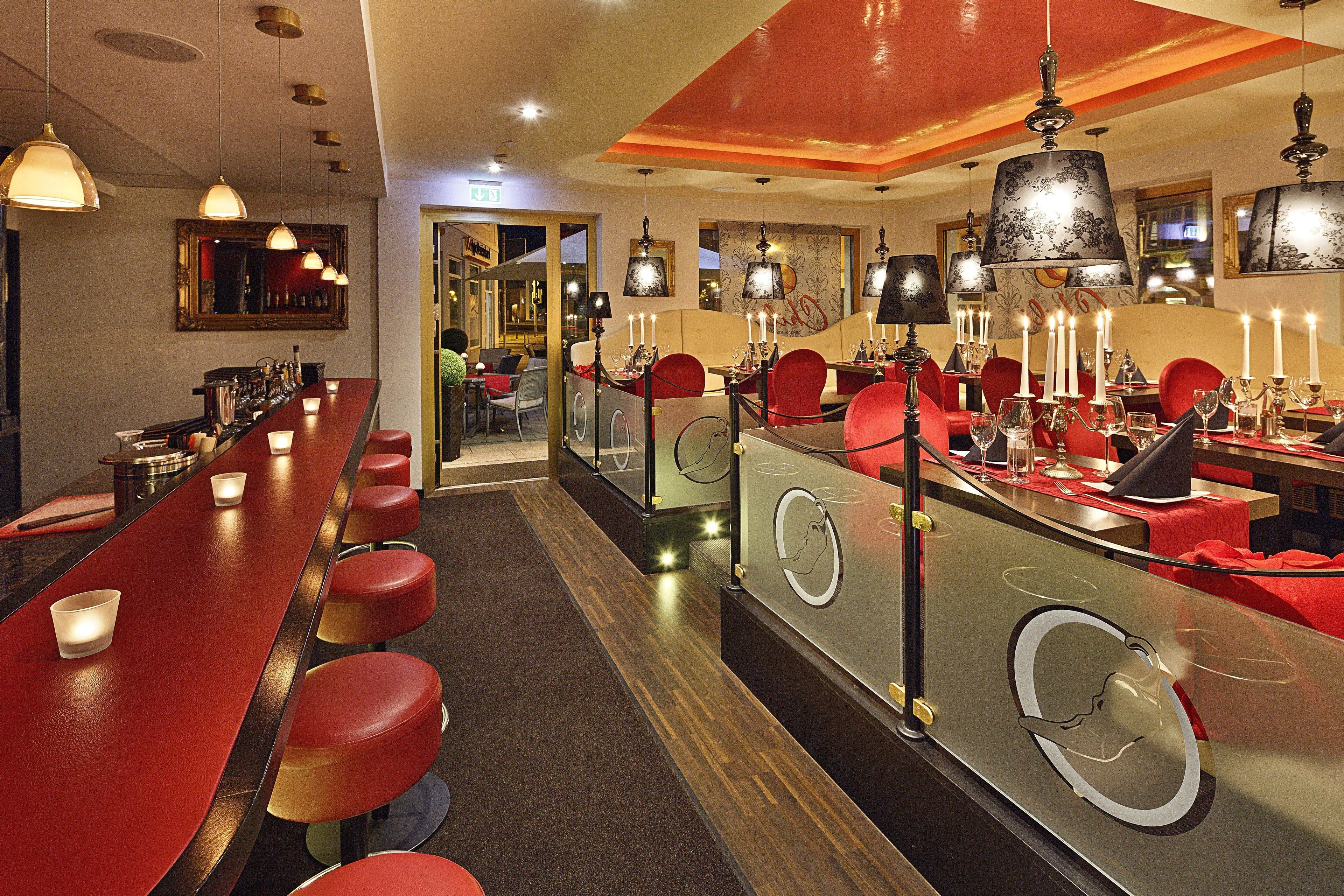 A bar area with red stools, a long counter, and multiple hanging lamps.