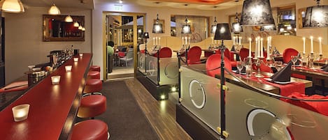 A bar area with red stools, a long counter, and multiple hanging lamps.