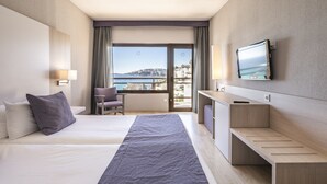 Habitación de hotel con cama, escritorio, silla, televisión y vista al mar.