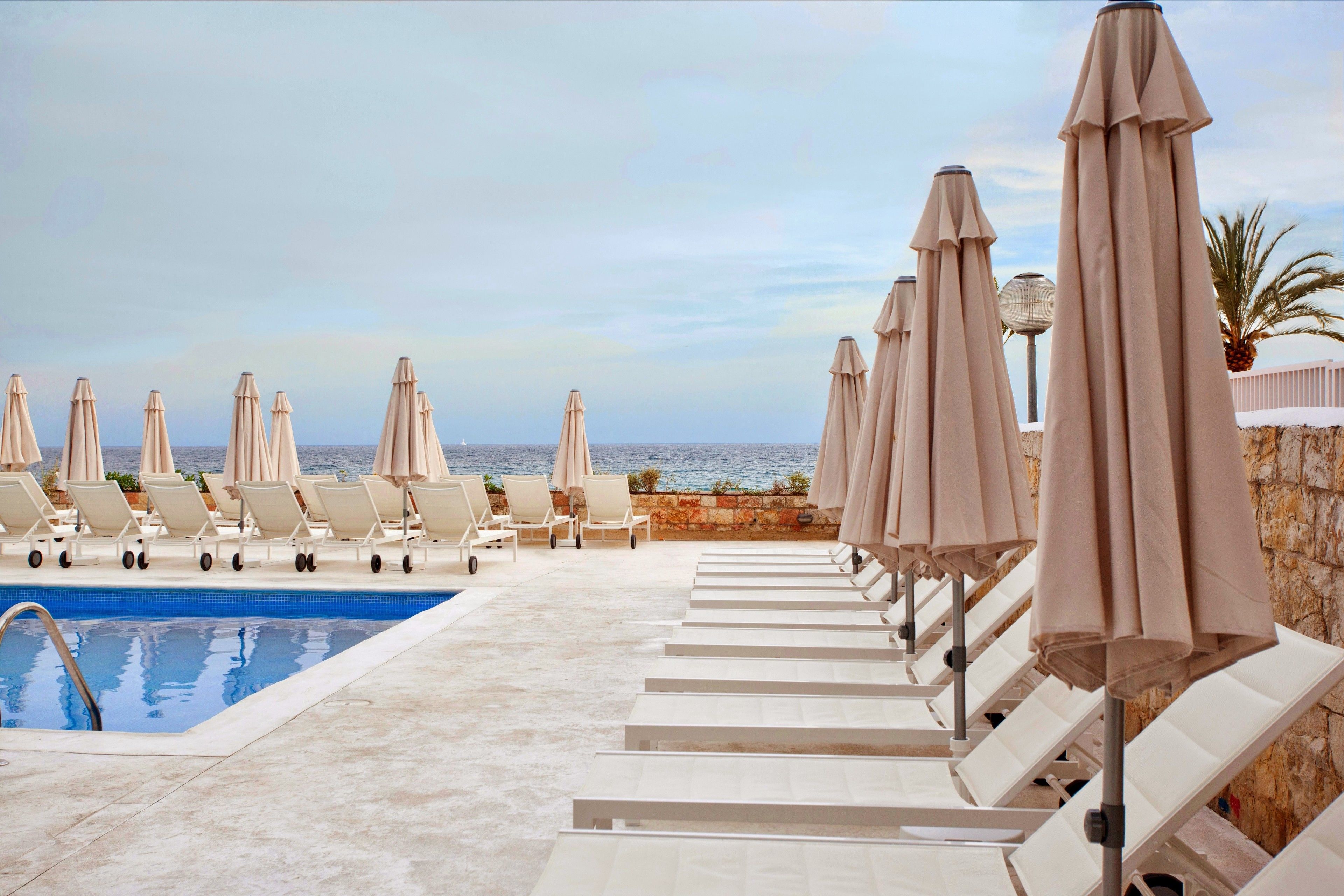 Zona junto a la piscina con sillones de descanso y sombrillas, vista despejada al mar y una pared de piedra.