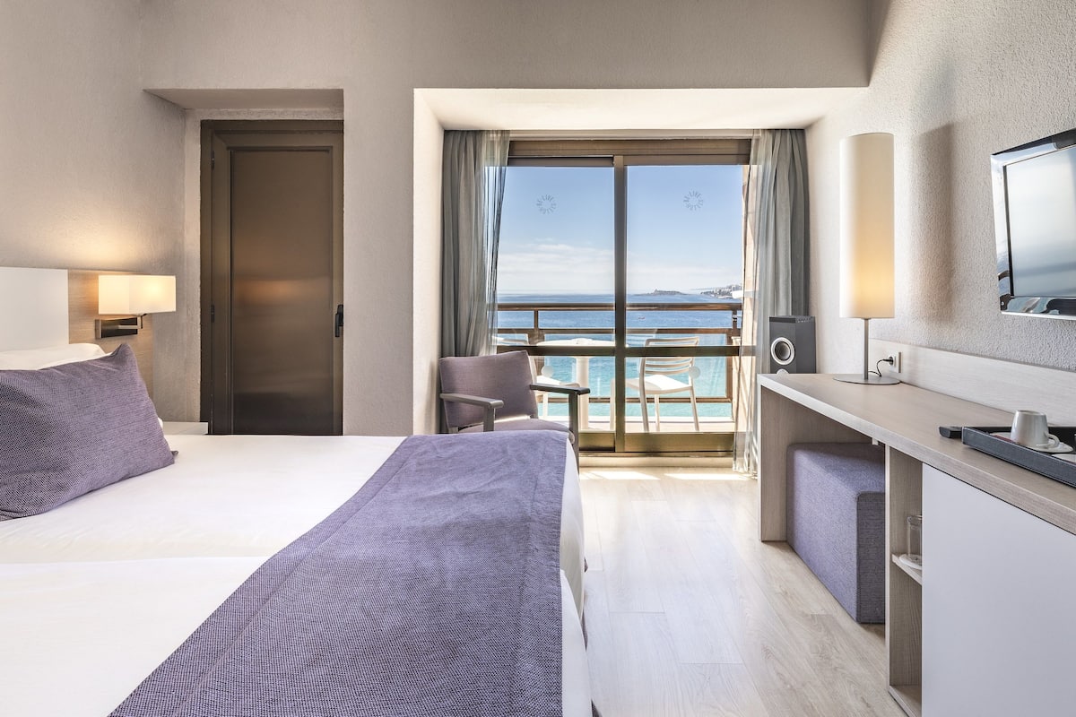 Habitación de hotel con cama, escritorio, televisor y vista al mar.