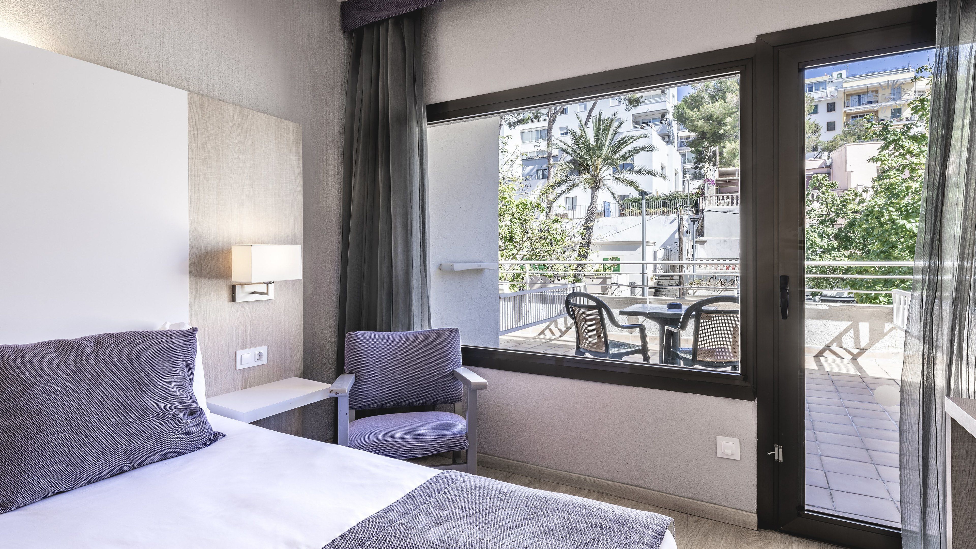Une chambre d’hôtel avec un lit, une chaise, une petite table et un balcon donnant sur la ville.