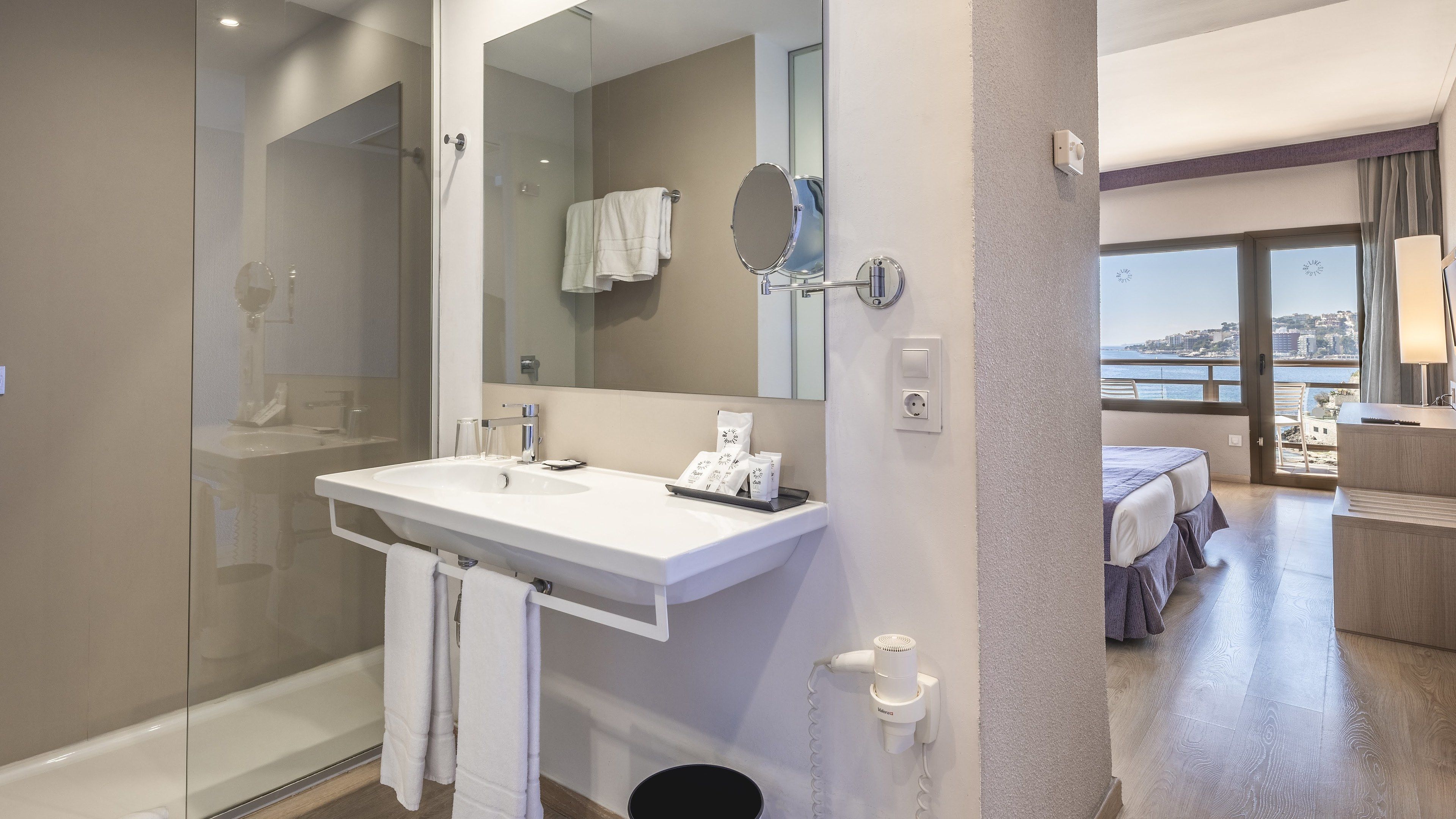 Un baño moderno con cabina de ducha de vidrio, un lavamanos blanco con tocador y un espejo grande.