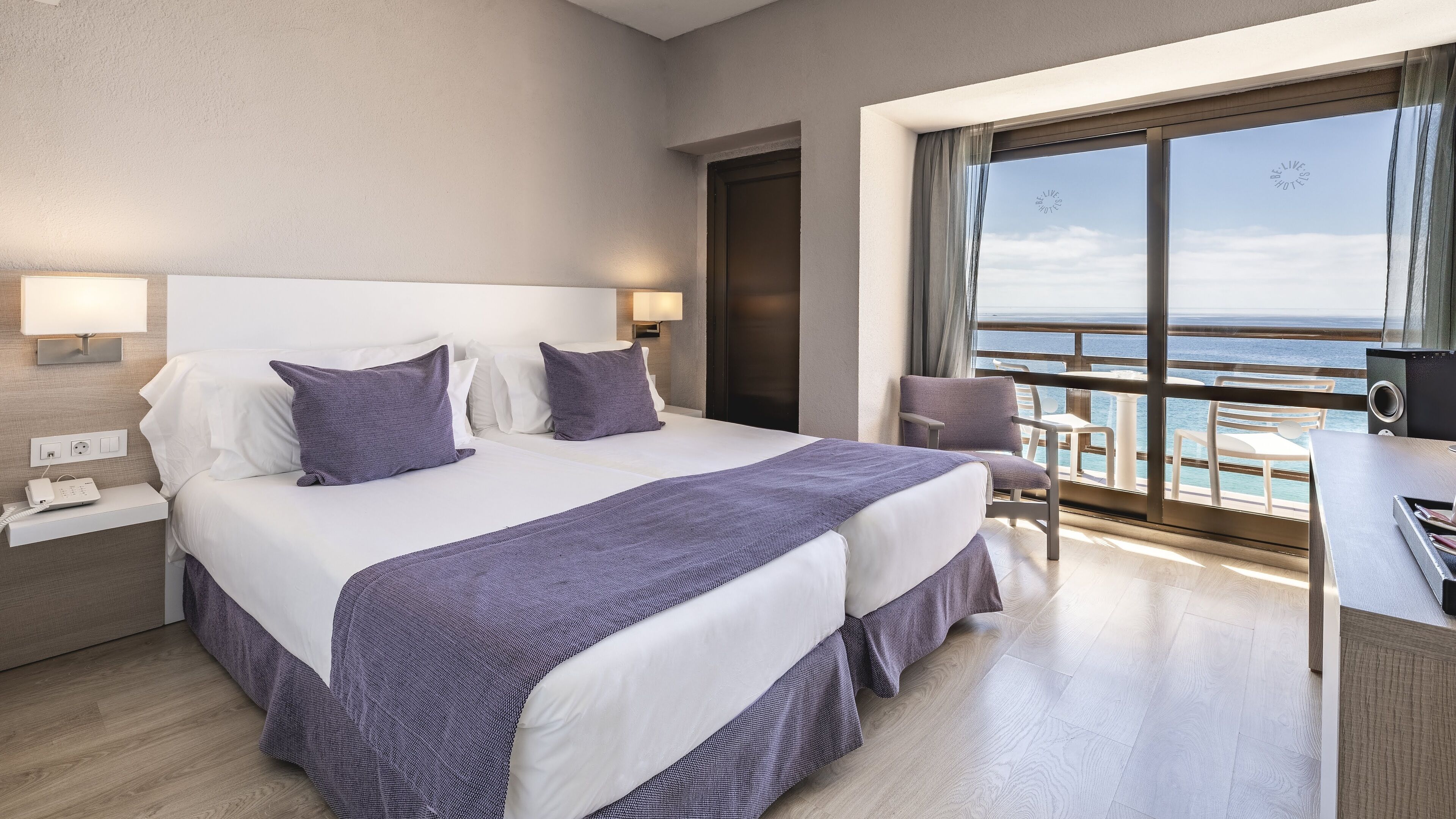 Ein Hotelzimmer mit einem großen Bett, zwei Nachttischen, einem Schreibtisch mit Stuhl und Meerblick.