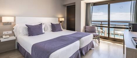 Ein Hotelzimmer mit einem großen Bett, zwei Nachttischen, einem Schreibtisch mit Stuhl und Meerblick.