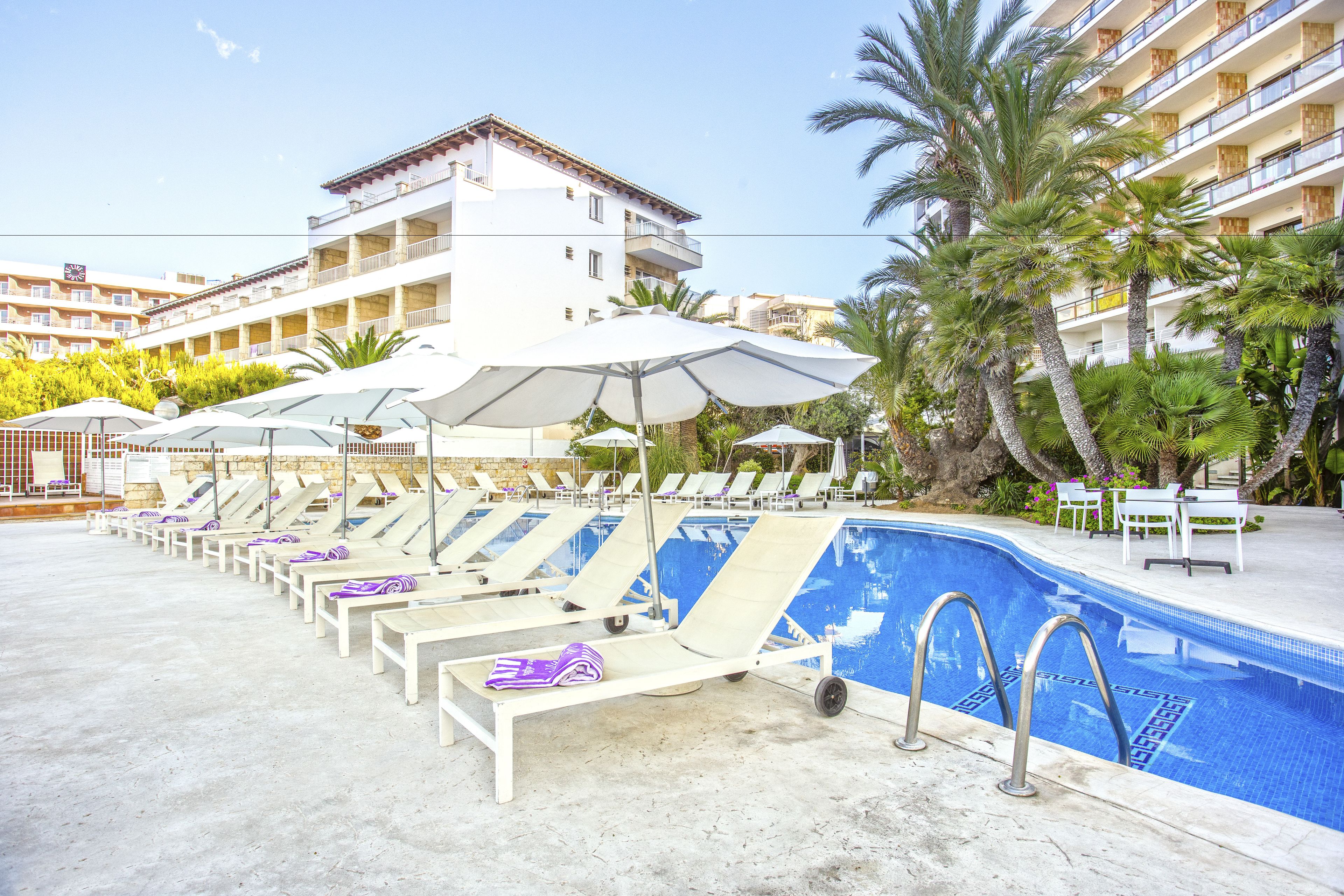 A poolside area with sun loungers, umbrellas, and a clear blue pool.