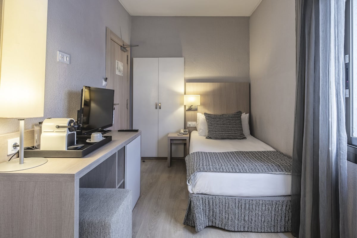 Una habitación de hotel con cama, mesita de noche, televisor y escritorio con cafetera.