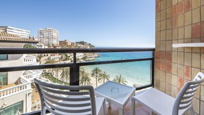 Un balcón con sillas y mesa blancos, con vistas a la playa y al paisaje urbano.