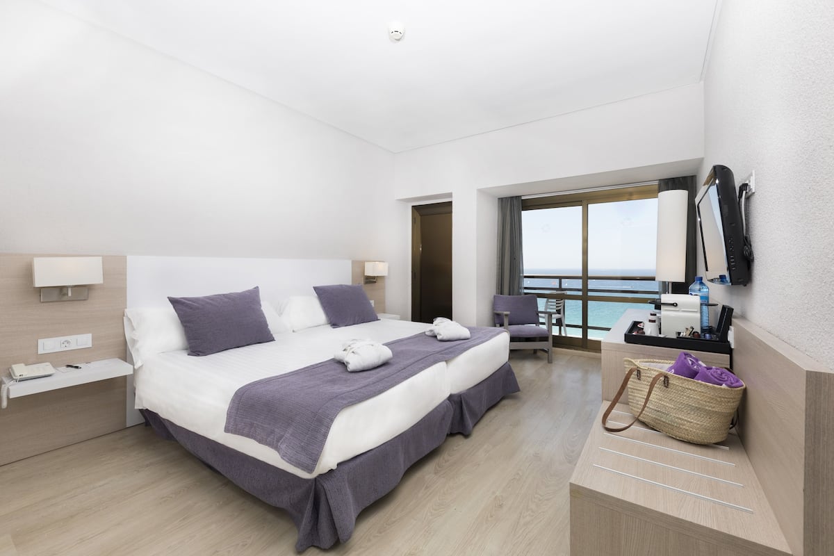 Una habitación de hotel moderna con una cama grande, un escritorio, una silla, un espejo de baño y vistas al mar.