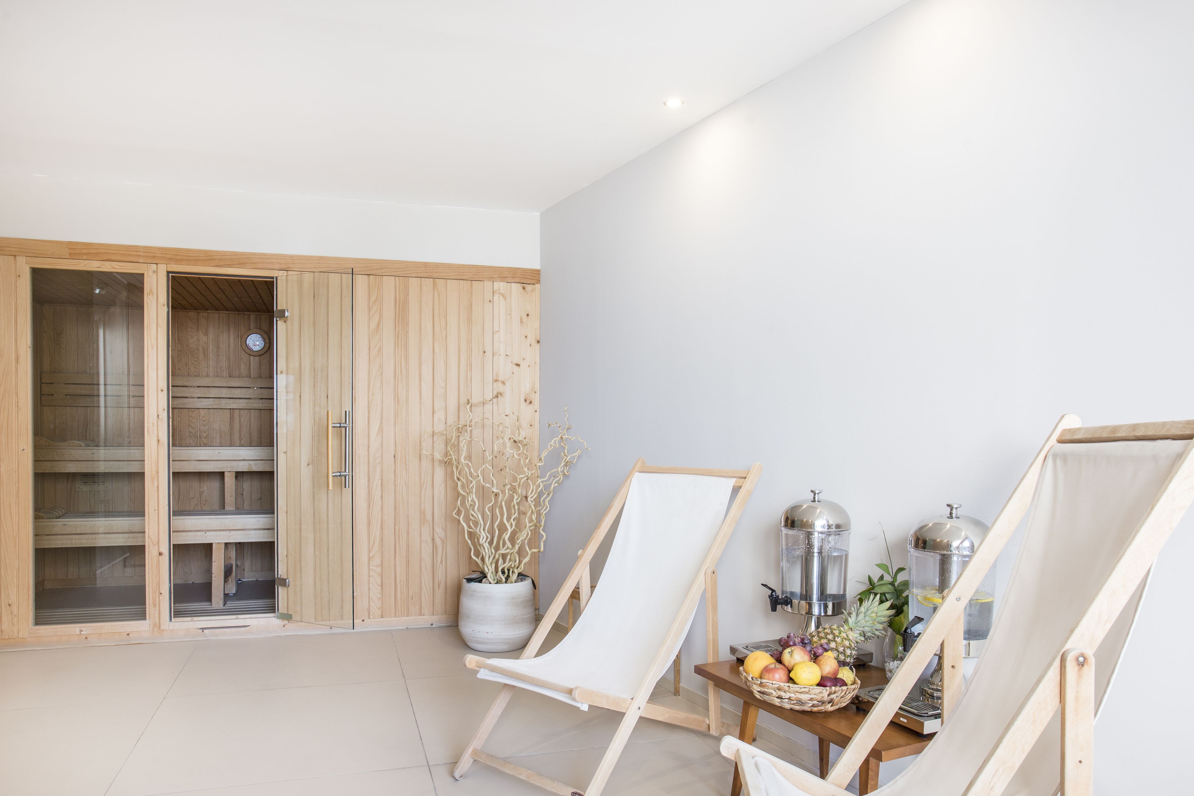 Una habitación con un armario de madera, una silla de lienzo blanca, una mesa con fruta y una planta en maceta.