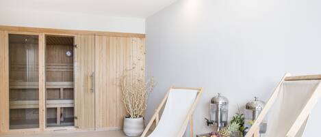 Una habitación con un armario de madera, una silla de lienzo blanca, una mesa con fruta y una planta en maceta.