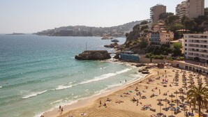 Un paisaje costero con playa arenosa, un promontorio rocoso y un puente.