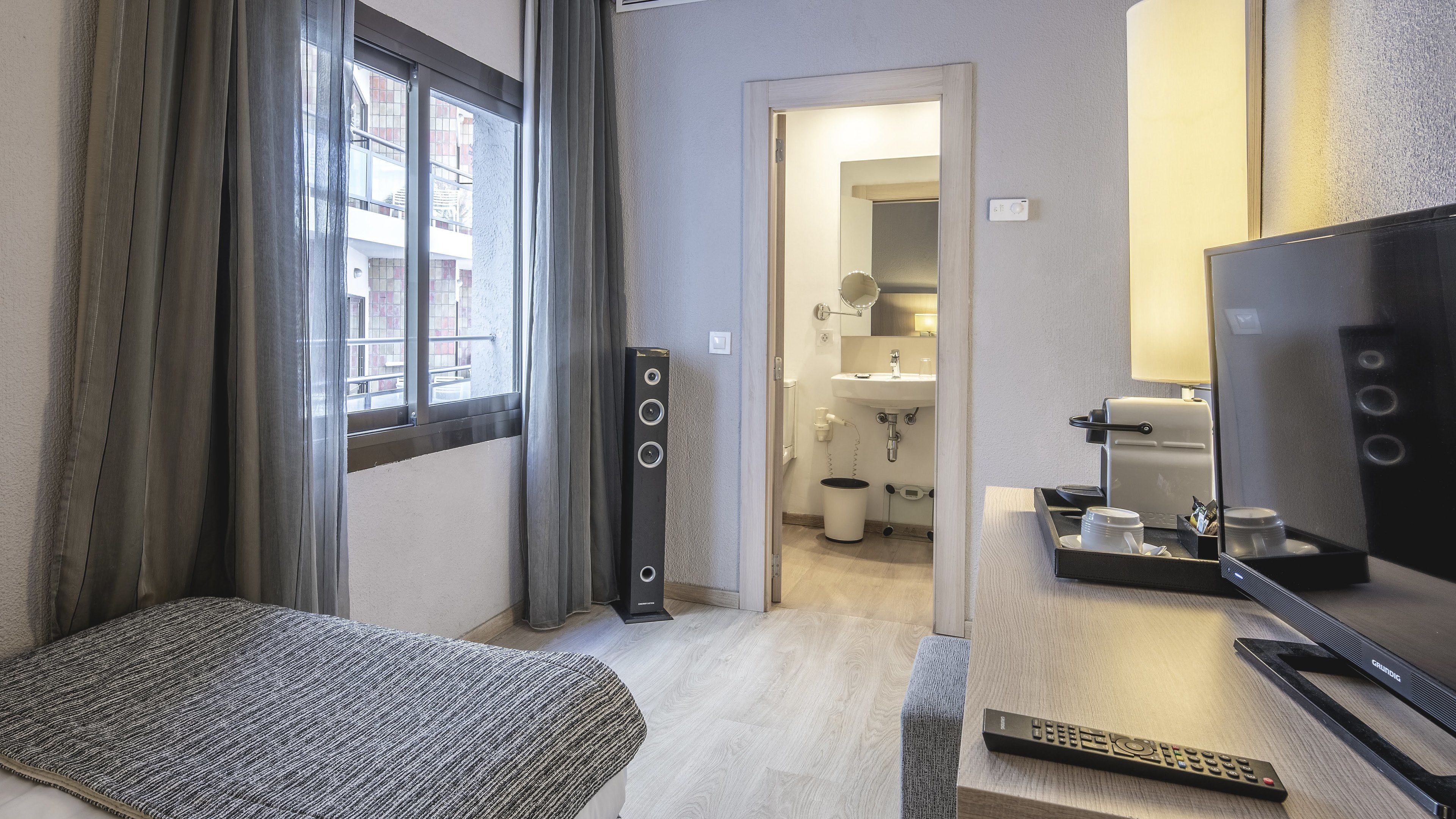 Habitación de hotel con cama, televisor, control remoto y baño visible a través de una puerta abierta.