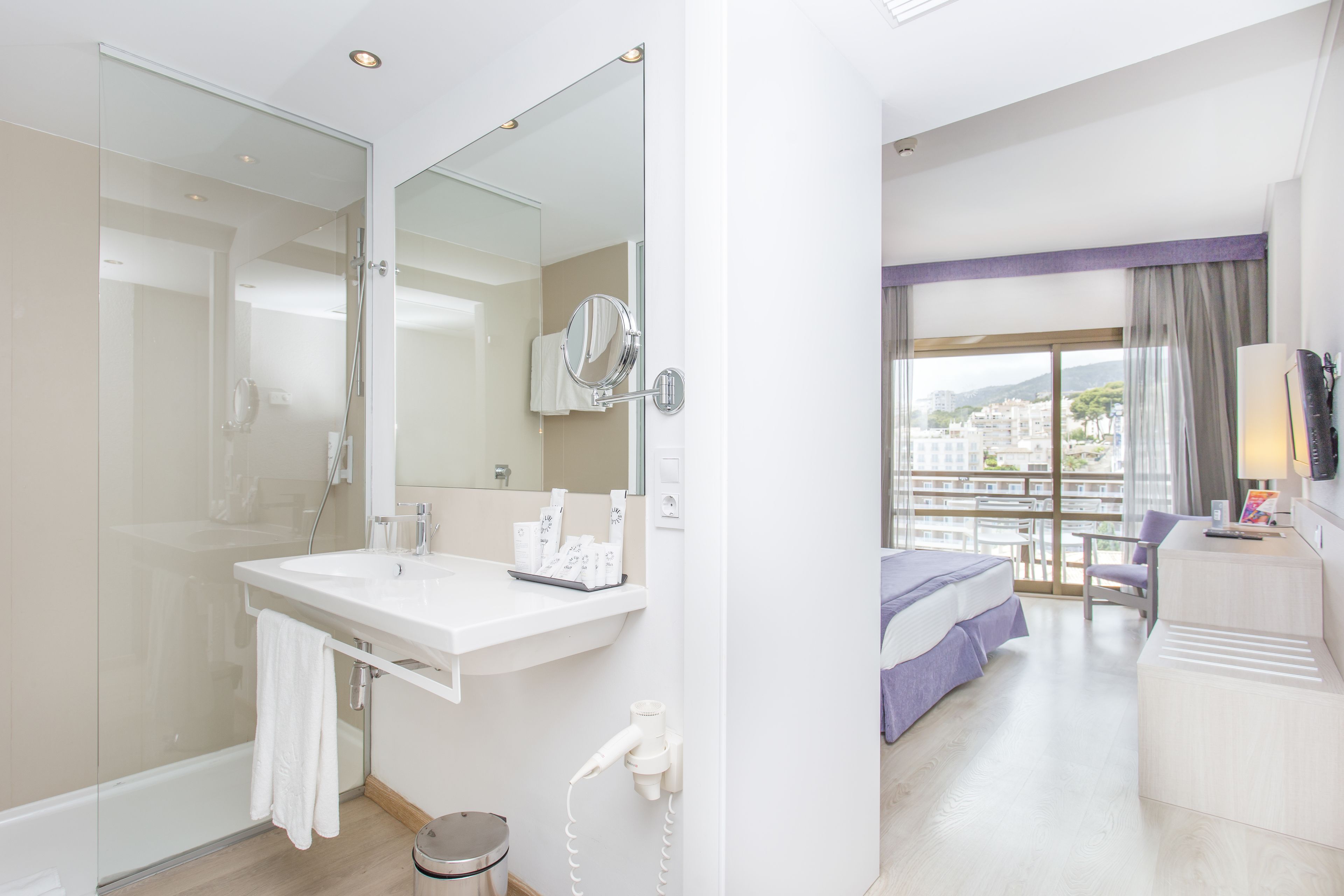 Una habitación de hotel moderna con un baño amplio, un balcón con vistas y una zona de dormitorio separada.