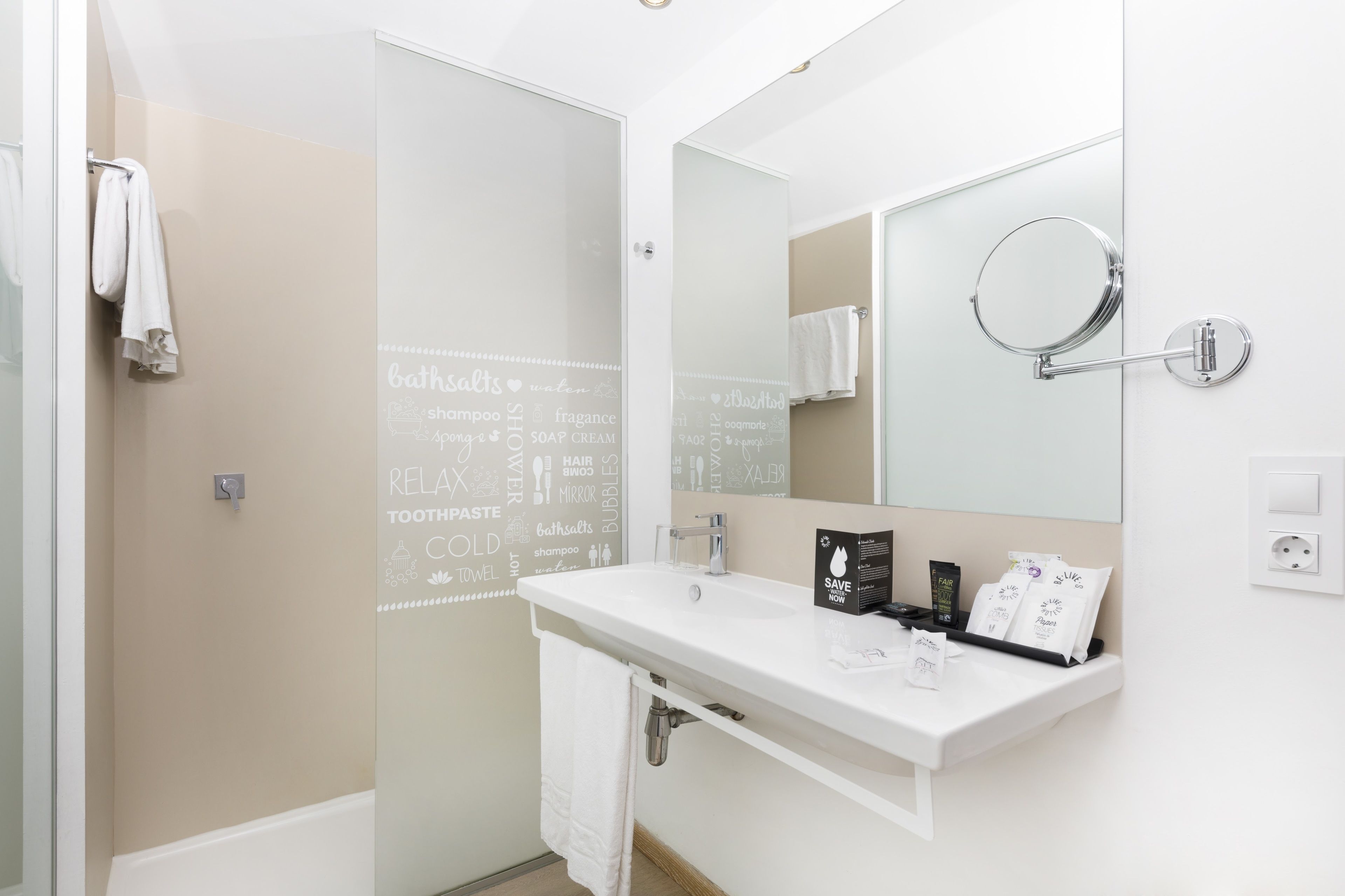 Un baño moderno con un lavabo blanco, un espejo grande y una puerta de ducha de cristal.