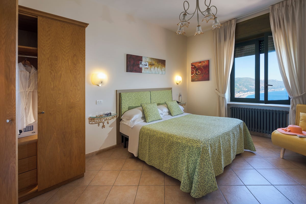 A bedroom with a bed, a wardrobe, a bedside table, a window with a view, and a chandelier.