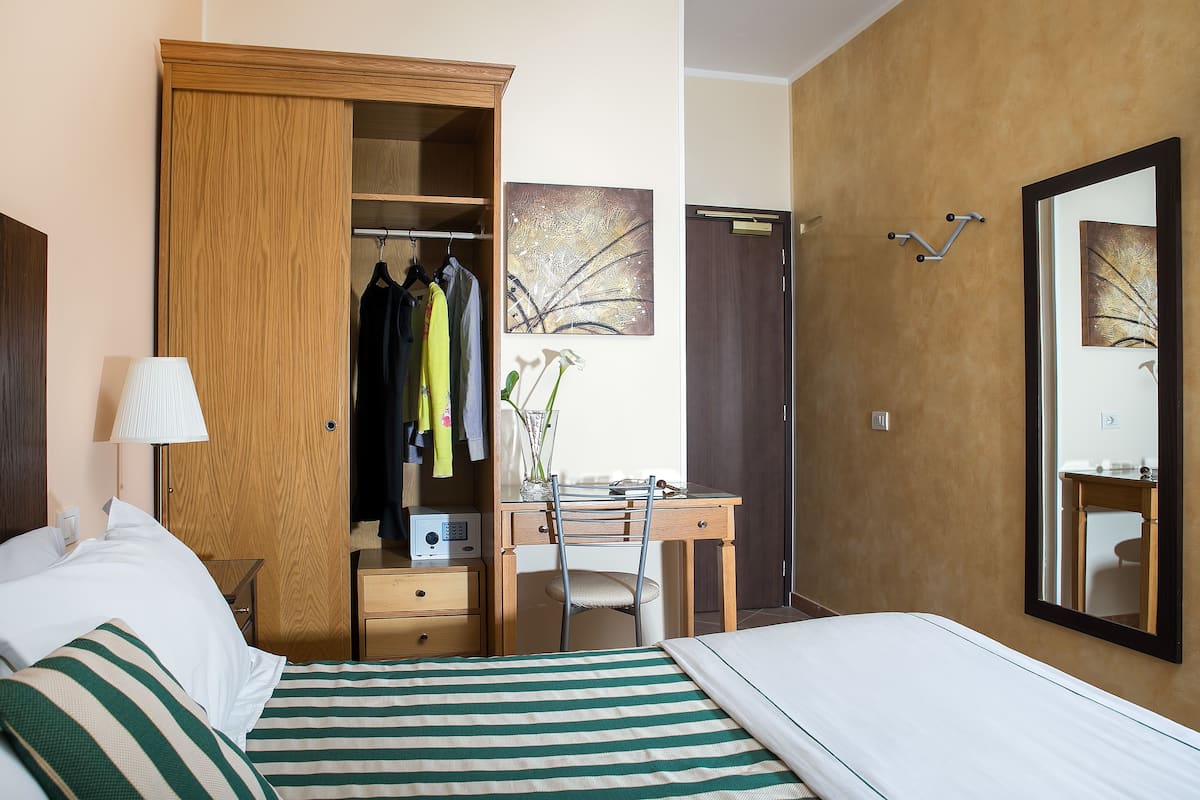A hotel room with a bed, a desk, a wardrobe, and a mirror.