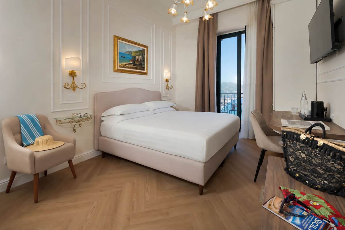 A hotel room with a bed, a chair, a desk, a television, and a window with a view.