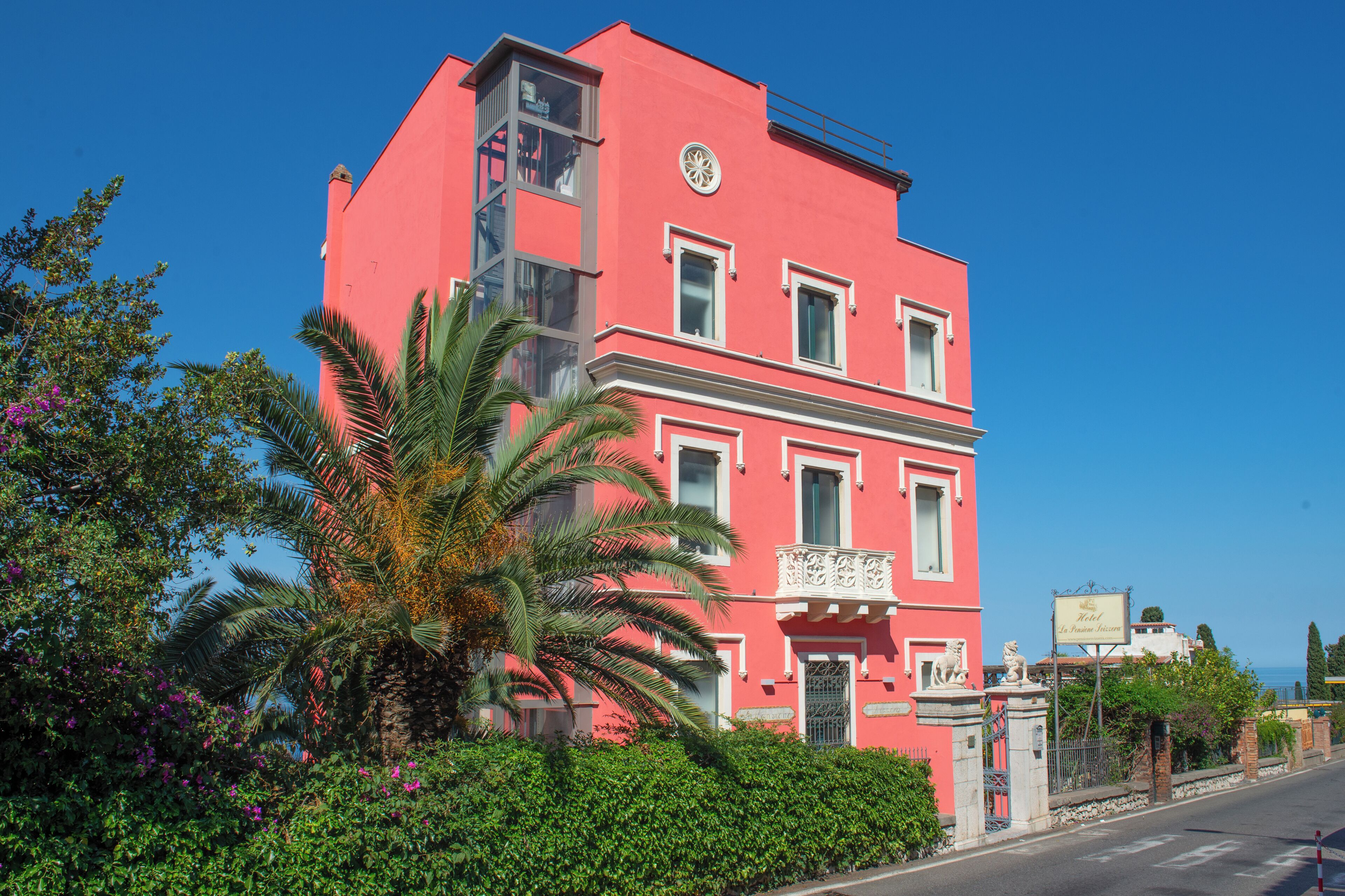 A pink building with a balcony, a palm tree, and a signboard.