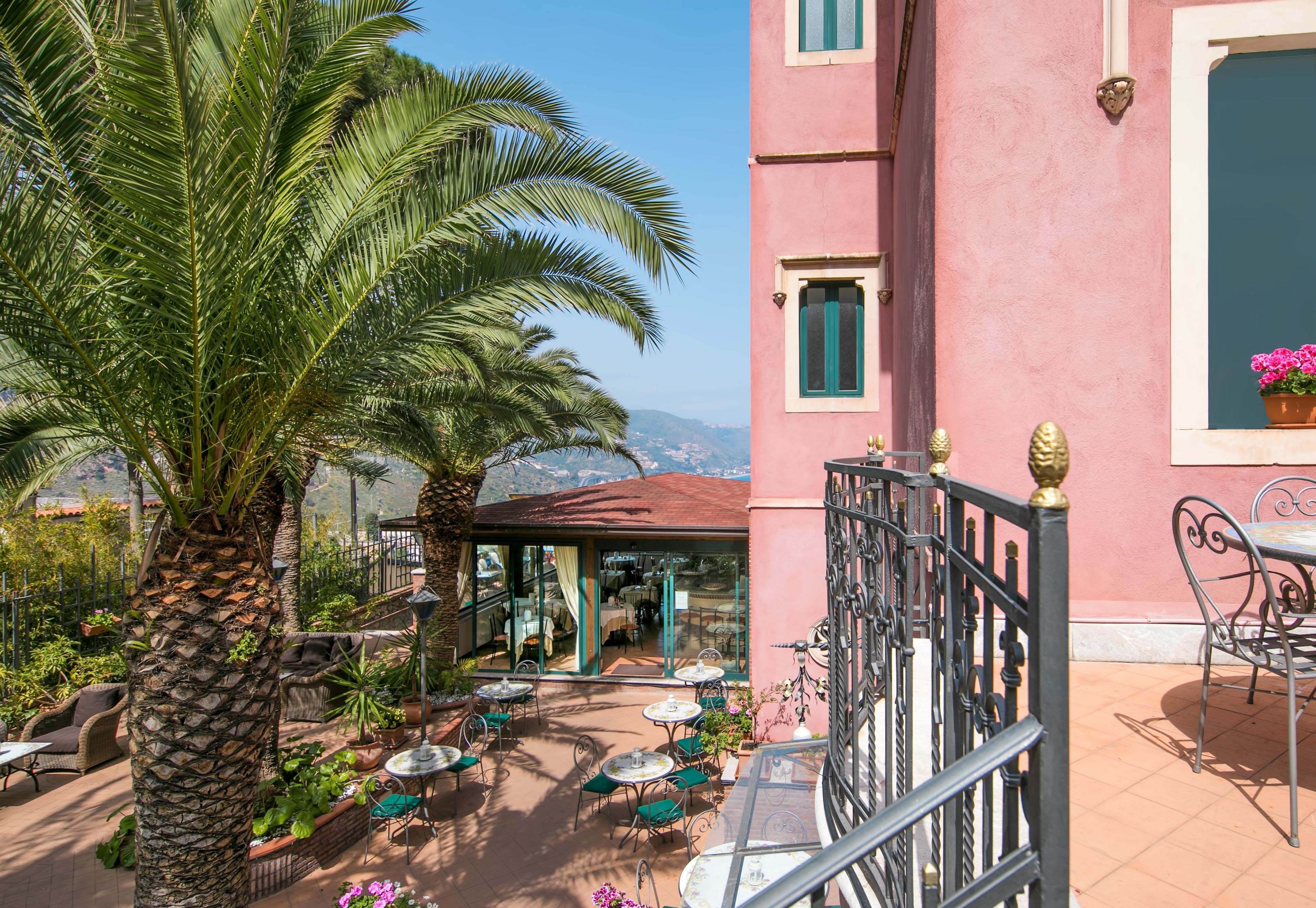 Un edificio rosa con un patio attrezzato con posti a sedere all'aperto, palme e vista sulle montagne.