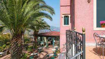 Un edificio rosa con un patio attrezzato con posti a sedere all'aperto, palme e vista sulle montagne.